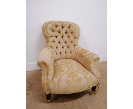 A 19th century button backed arm chair upholstered in yellow floral fabric, raised on brass castors.