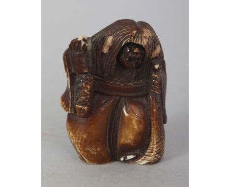 AN EARLY 20TH CENTURY JAPANESE STAINED IVORY NETSUKE OF A ROBED DEMON, with long hair and fierce expression, and clasping two