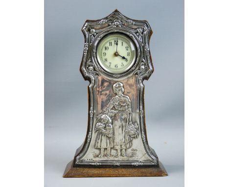 A SILVER FRONTED OAK MANTEL CLOCK, the shaped case housing an enamel dial with Arabic numerals, the silver with floral swag d