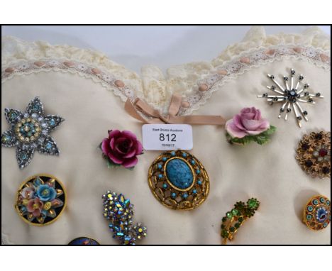 A heart shaped pad / cushion adorned with several vintage and retro costume jewellery brooches of various designs, please ref