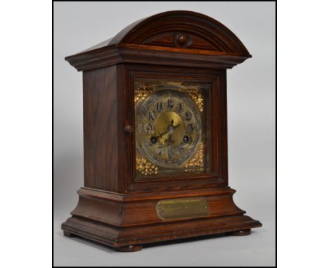 An oak mantel clock having dome top with a bevelled bezel and a silvered and gilt face, the clock is raised on bun feet and h