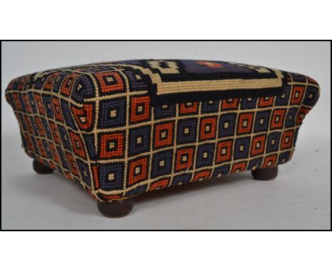 A Victorian /  early 20th century tapestry upholstered footstool in the sarcophagus form being raised on bun feet